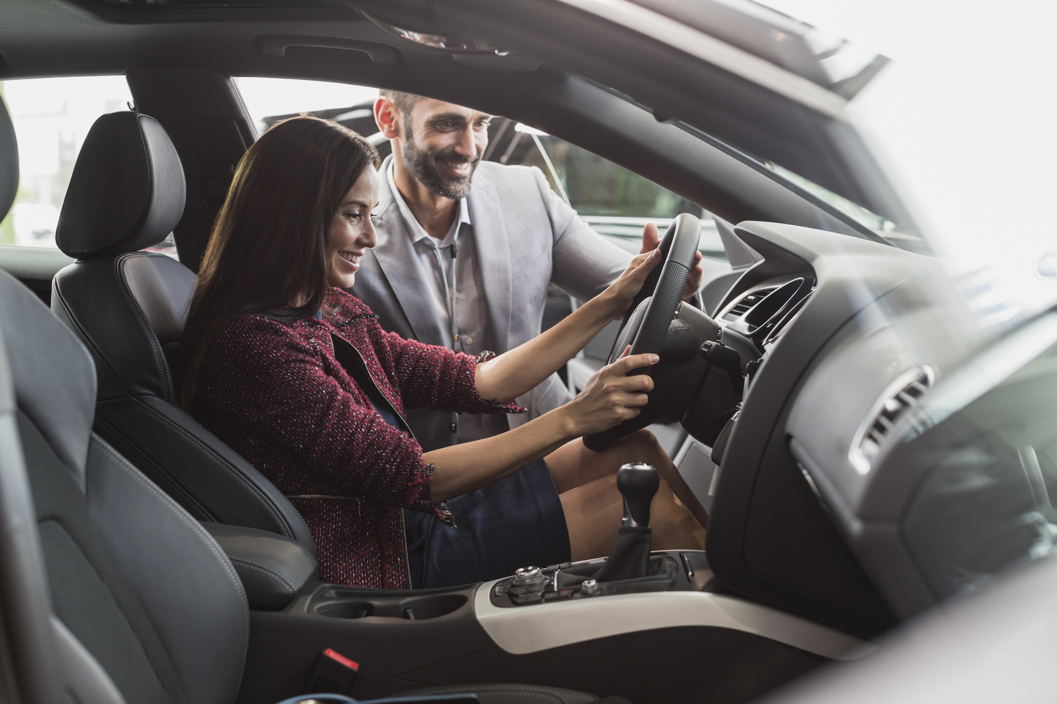 Car salesman and female customer in driverÍs seat of new car in car dealership showroom